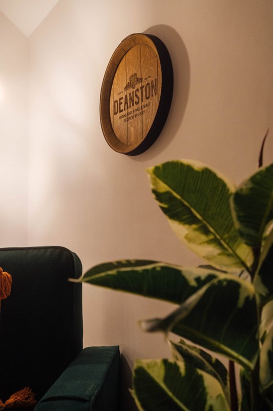 Wall-mounted wooden clock with plant and dark upholstered furniture visible