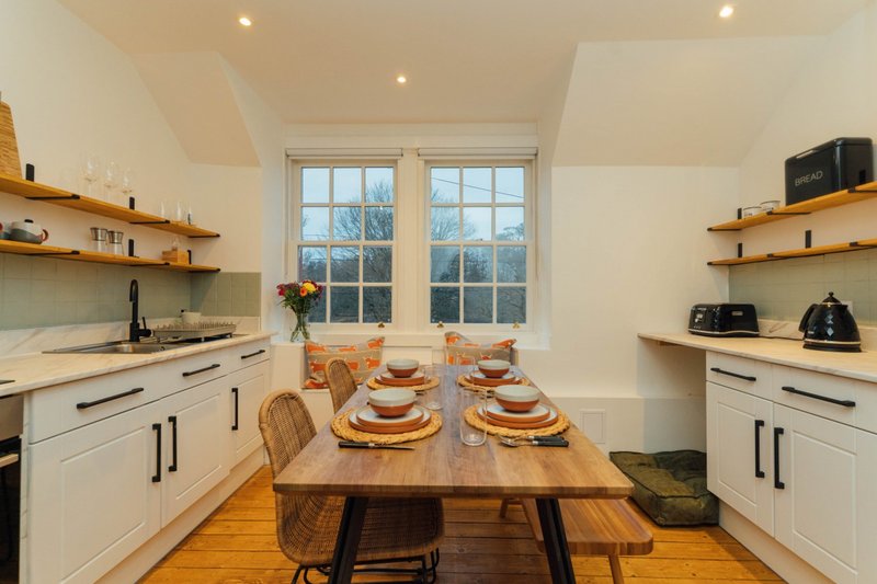 Modern kitchen with white cabinetry, wooden dining table set for two, and large windows