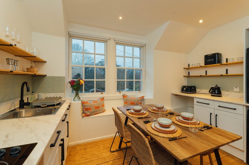 Bright kitchen diner with wooden table, two place settings, white cabinetry and large windows