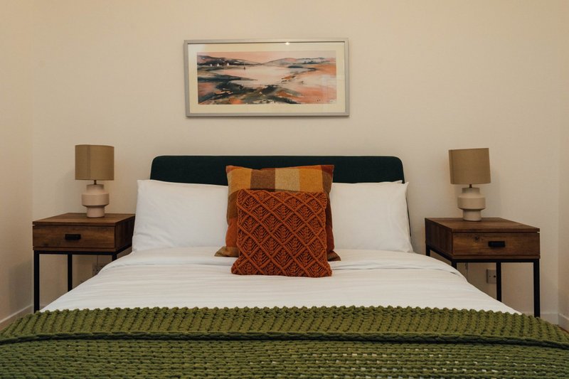 Bedroom with double bed, white bedding, decorative pillows, wooden nightstands with lamps, and framed artwork above headboard
