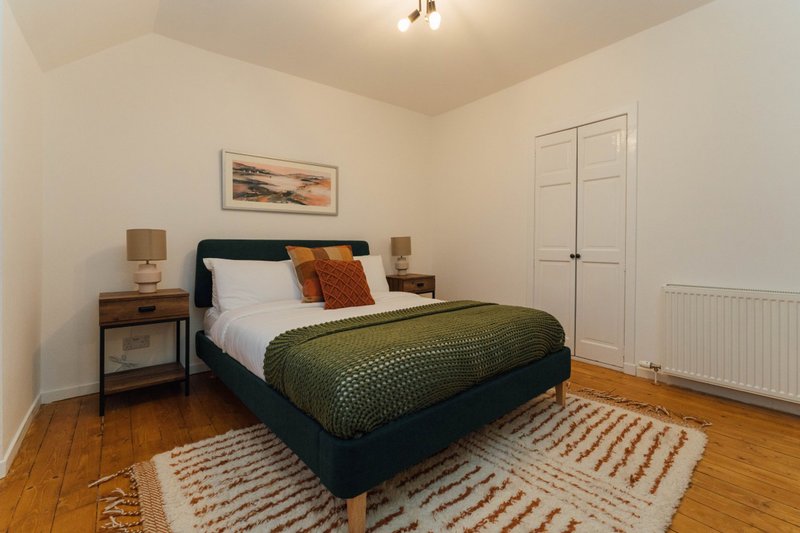 Bedroom with double bed, wooden nightstands, striped rug, and white wardrobe doors