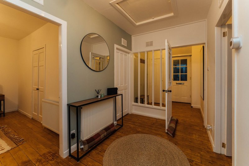 Spacious hallway with wooden flooring, yellow doors, round mirror and console table