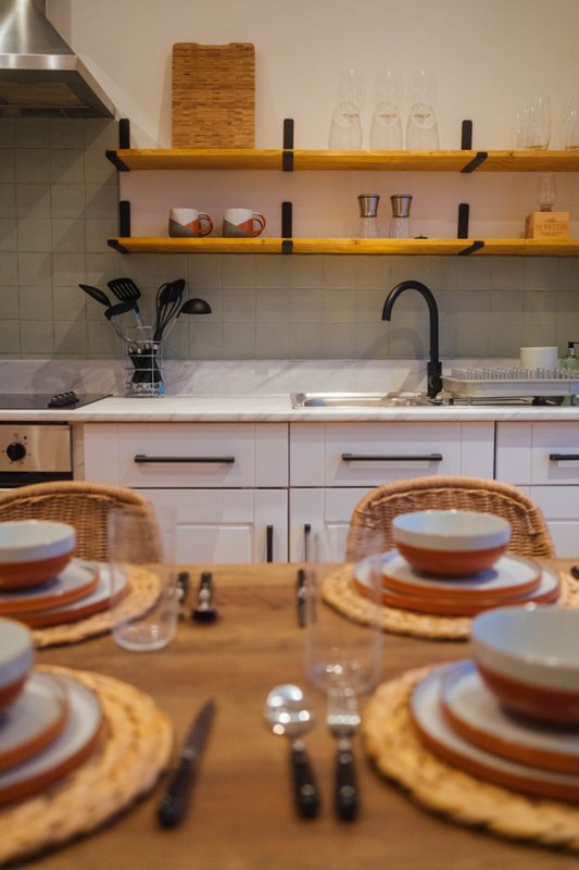 Modern kitchen with wooden shelves, white cabinetry, black faucet, and dining table set for four