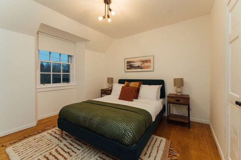 Bright bedroom with queen bed, wooden floors, bedside tables and window view