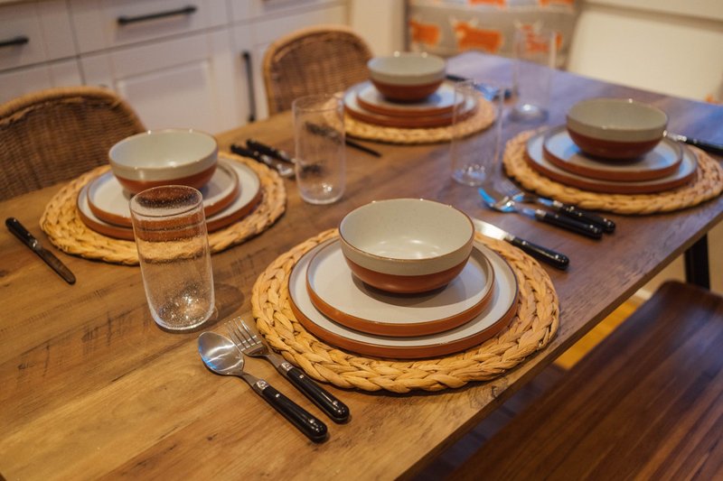 Dining table set with place settings, woven placemats, stacked bowls and glasses