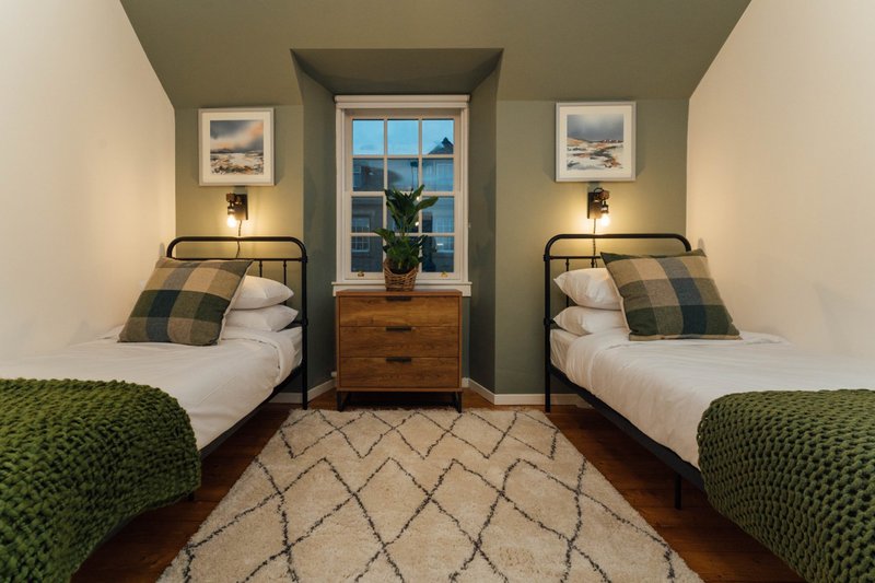 Twin bedroom with two single beds, wooden dresser, window with sea view, framed artwork