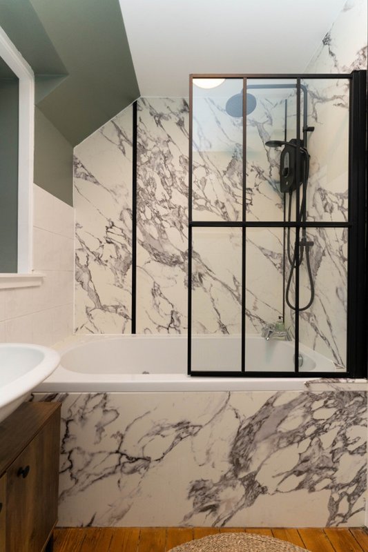 Modern bathroom with marble-patterned wall tiles, black-framed glass shower enclosure, and white sink