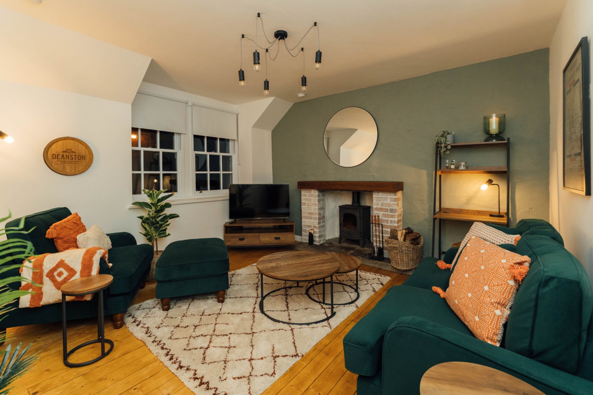 Living room with green sofas, fireplace, TV, round mirror, and orange accent pillows
