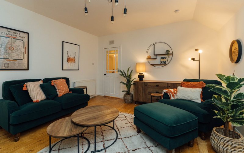 Modern living room with dark teal sofa, ottoman, wooden coffee table and indoor plants