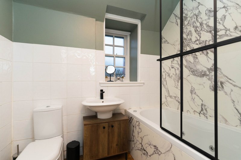 Modern bathroom with white tile walls, marble shower enclosure, wooden vanity and toilet