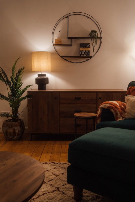 Bedroom with wooden furniture, lamp, circular wall shelf, and green upholstered chair
