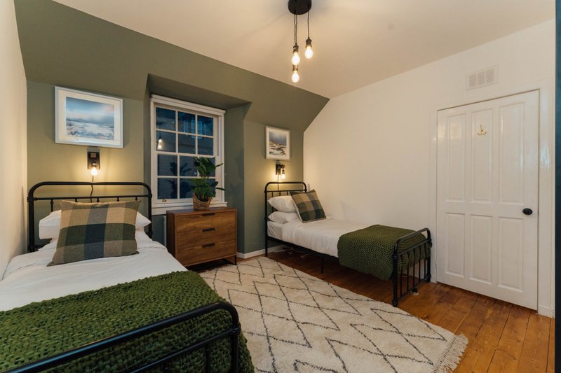 Bedroom with two single beds, wooden dresser, green wall, and window with nightstands