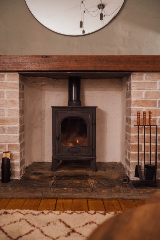 Living room fireplace with black wood-burning stove, brick surround, and circular mirror above