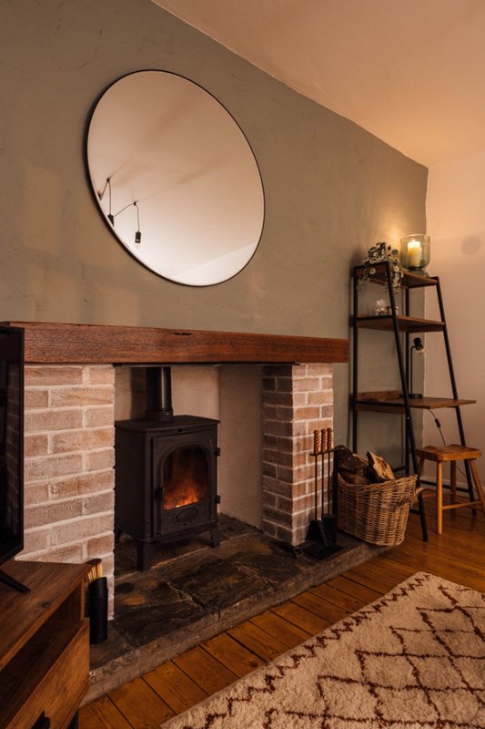 Living room with fireplace, wood-burning stove, round mirror and wooden floor