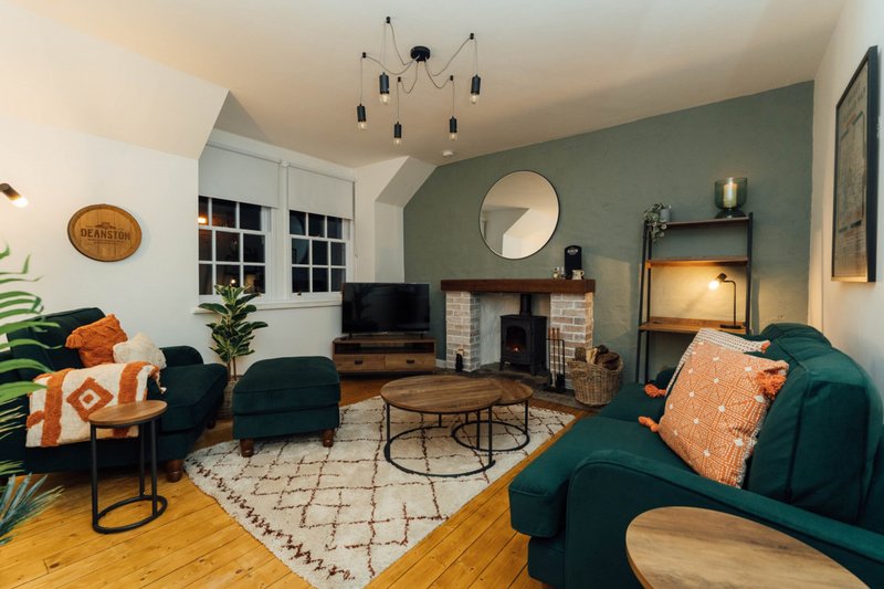 Living room with teal sofas, fireplace, round mirror, pendant lighting and wooden flooring