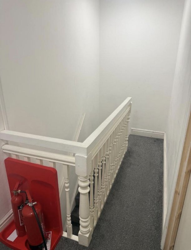 Staircase landing with white banister, gray carpet runner, and red fire extinguisher