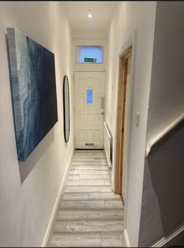 Narrow hallway with white walls, wooden flooring, wall-mounted artwork and doors