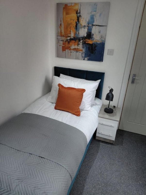 Modern bedroom with single bed, orange cushion, abstract wall art and bedside table