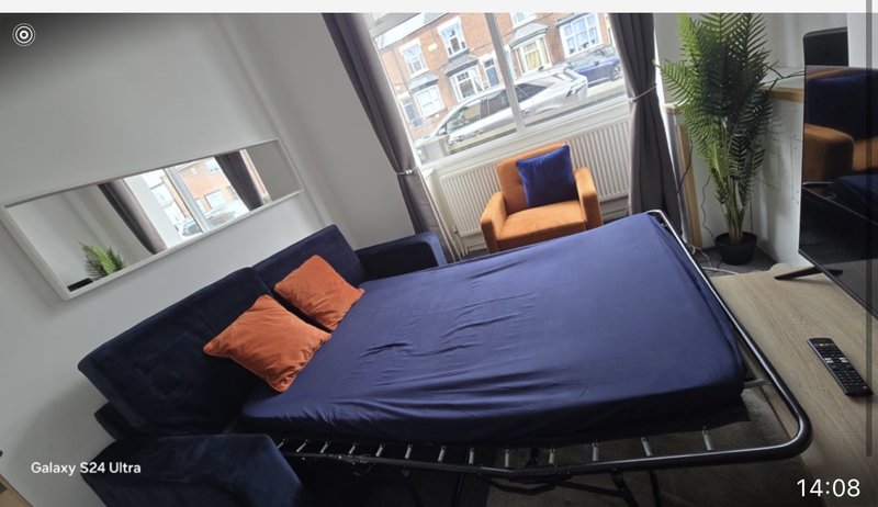 Bright bedroom with double bed, orange cushions, windows with street views and potted plant