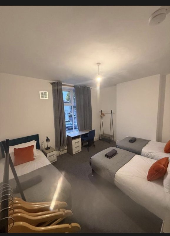 Bedroom with two single beds, desk, chair, window with curtains and ceiling light