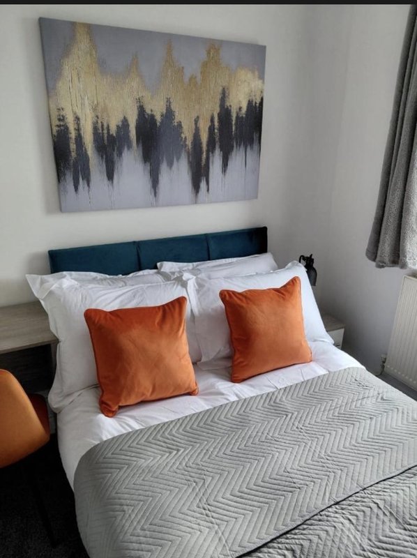 Modern bedroom with double bed, orange cushions, grey patterned bedding and abstract wall art