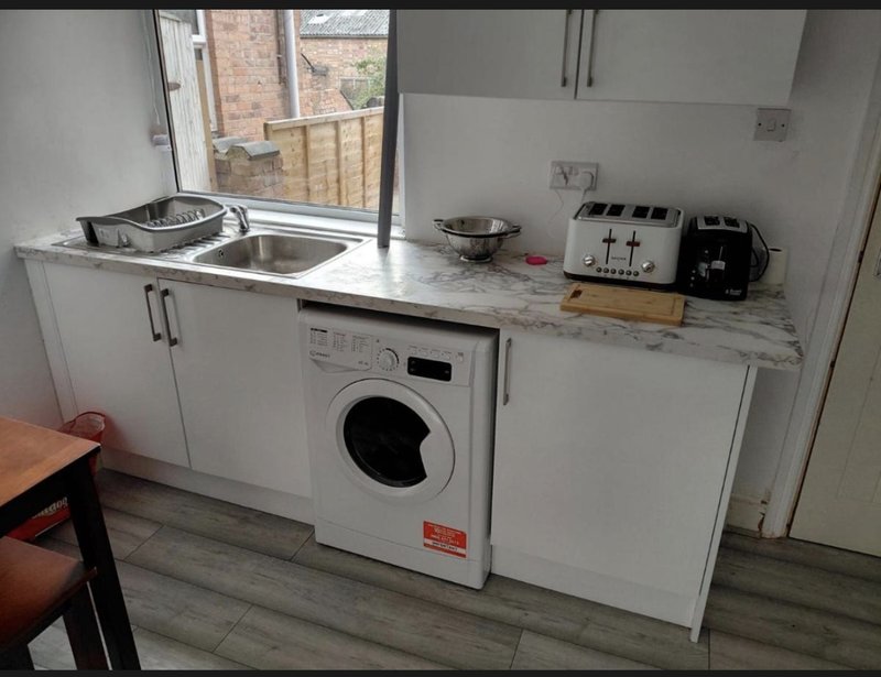 Compact kitchen with washing machine, sink, countertop appliances and window overlooking brick buildings