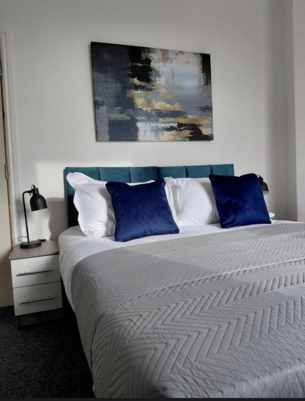Modern bedroom with teal headboard, white bedding, navy cushions and abstract wall art