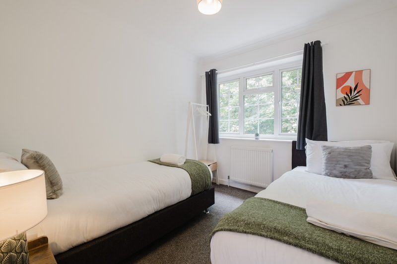 Bright twin bedroom with two single beds, green throws, window with black curtains, wall art