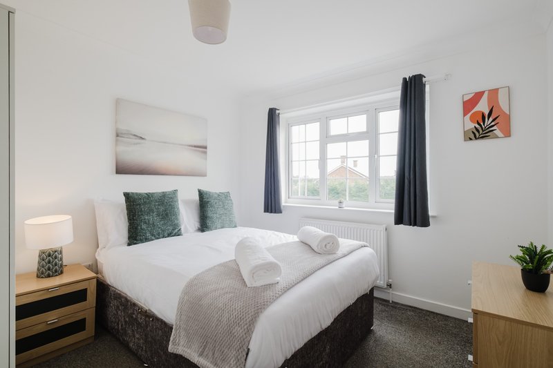 Bright bedroom with double bed, white bedding, green cushions, dark curtains and wall art