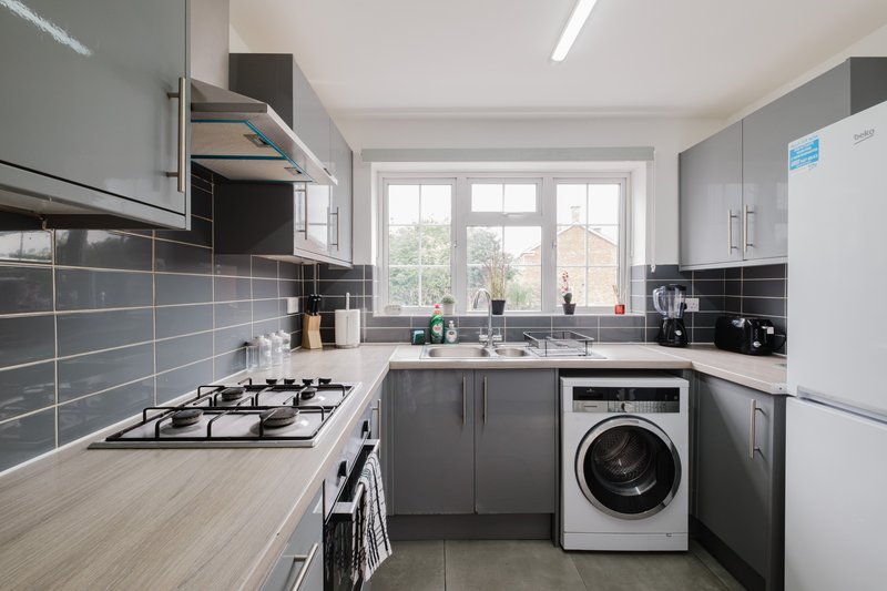 Modern kitchen with gray cabinets, gas hob, washing machine, and window overlooking garden