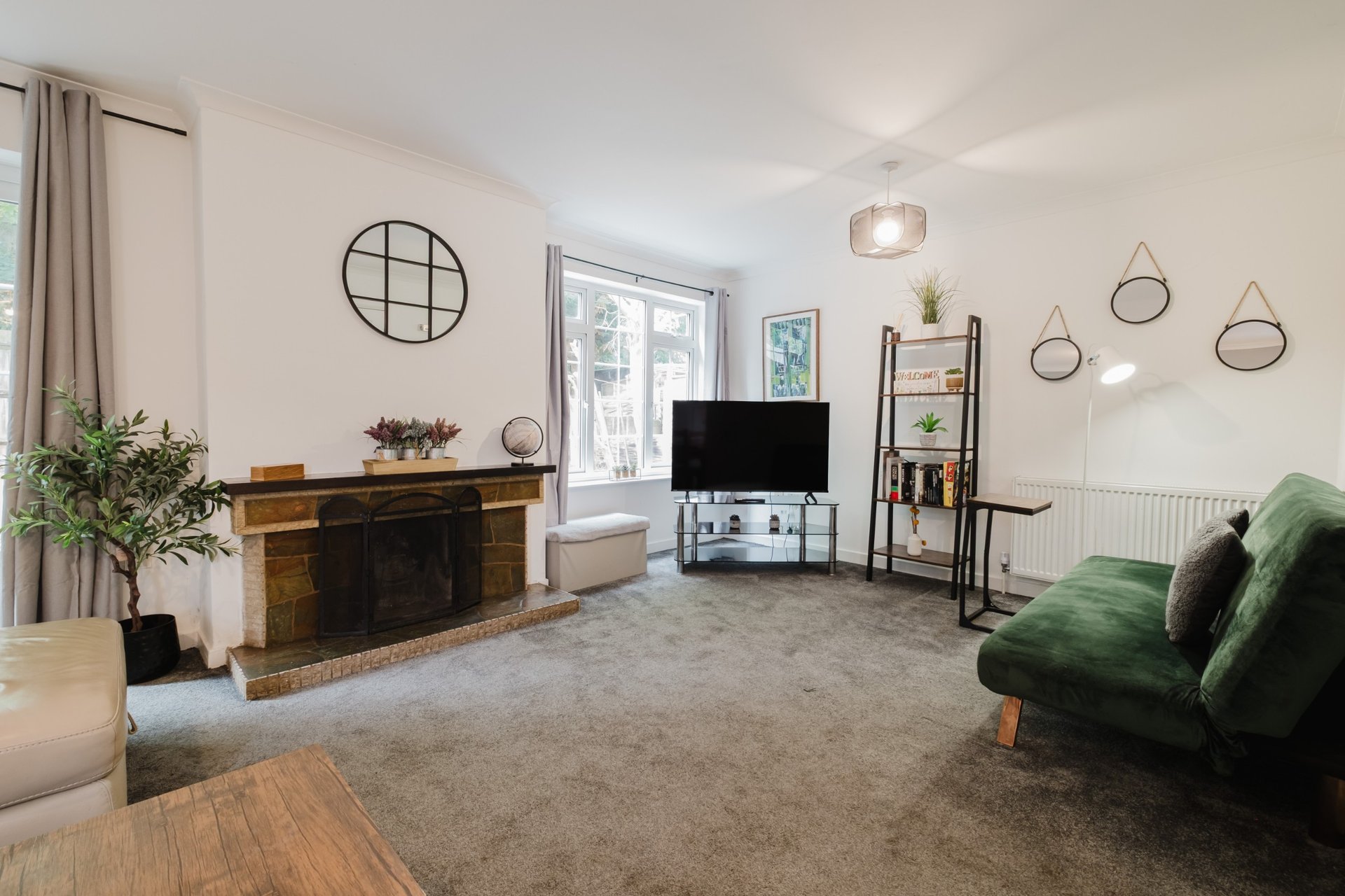 Bright living room with fireplace, green sofa, TV stand, and decorative wall mirrors