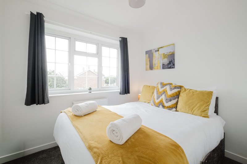Bright bedroom with double bed, yellow bedding, white pillows, large window and dark curtains