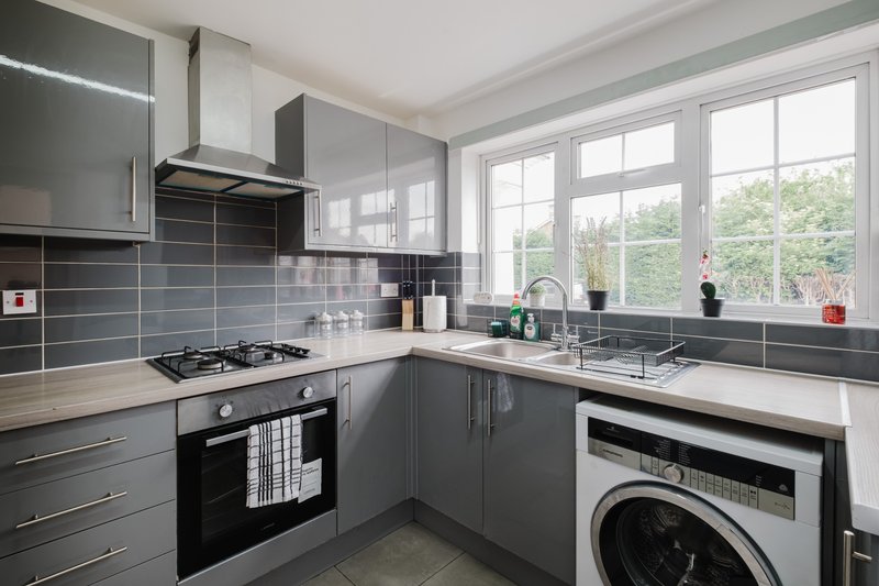 Modern kitchen with dark grey cabinetry, gas hob, black oven, washing machine and large window