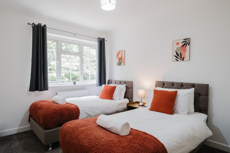 Bright bedroom with two single beds, orange cushions, white bedding, and window with black curtains