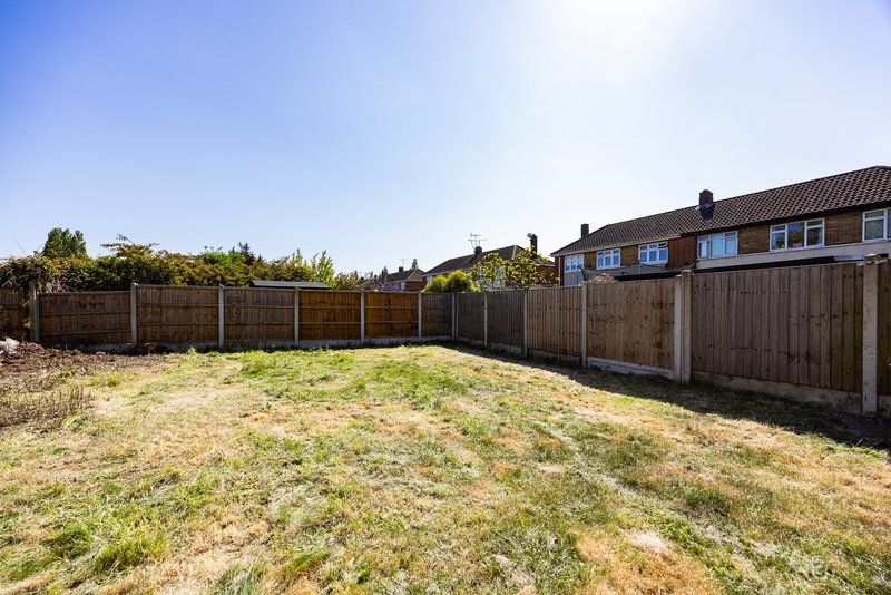 Suburban garden with wooden fencing, grass lawn and brick house in background