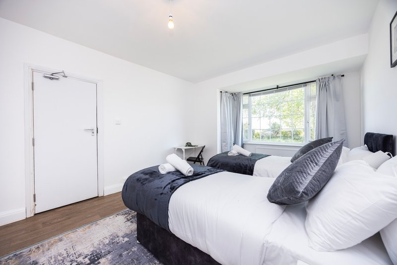 Bright bedroom with twin beds, white bedding, grey pillows and wooden flooring