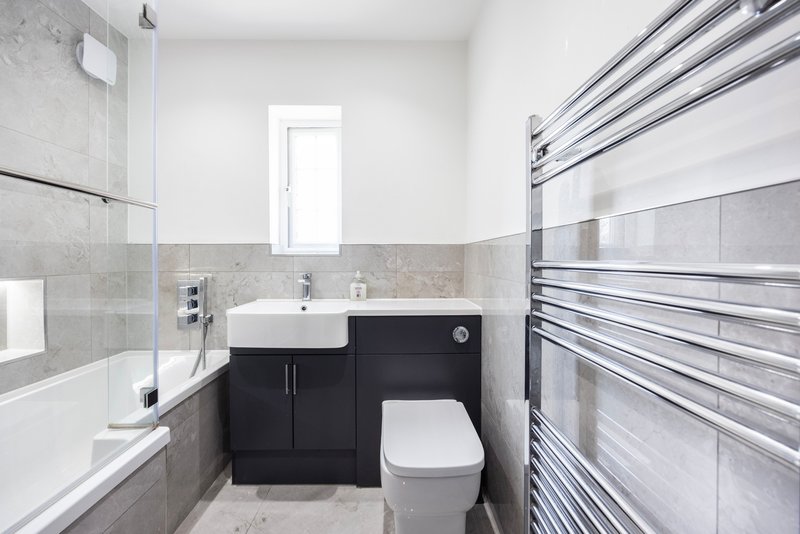 Modern bathroom with black vanity, white sink, toilet, and heated towel rack