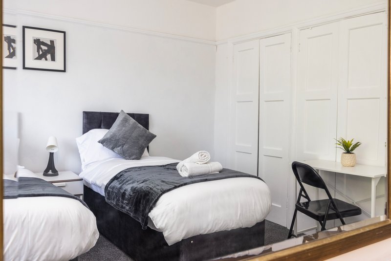 Modern bedroom with two single beds, white bedding, gray pillows, wooden desk and black chair