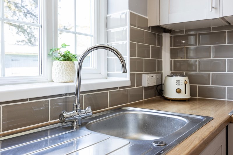 Modern kitchen with stainless steel sink, chrome faucet, brown subway tile backsplash and window
