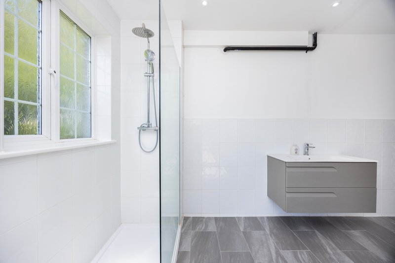 Modern bathroom with walk-in shower, gray vanity, window and white tile walls
