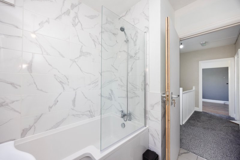 Modern bathroom with marble-effect tiled walls, glass shower enclosure and white bathtub