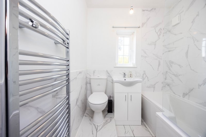 Modern bathroom with marble-effect tiles, heated towel rail, toilet, pedestal sink and window