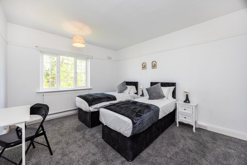 Bright bedroom with two single beds, white walls, large window, grey carpet and bedside table