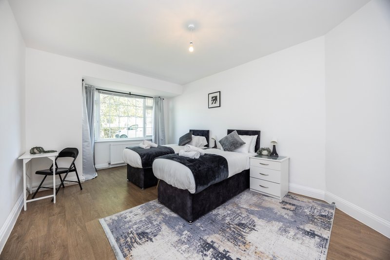 Bright bedroom with two single beds, wooden floor, window and white walls