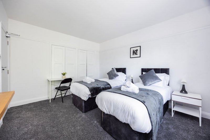 Bright bedroom with two single beds, white bedding, grey carpet and minimalist furnishings