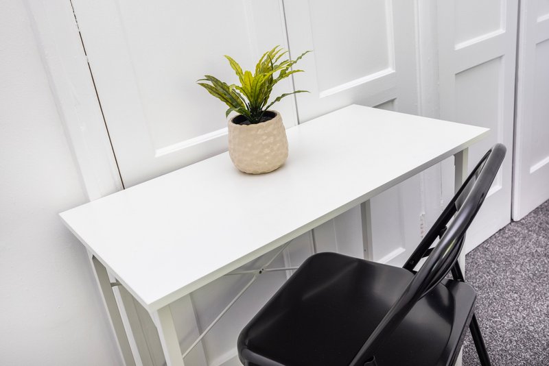White desk with potted plant, black chair, and bright window in minimalist room