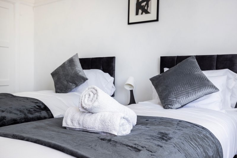 Modern bedroom with two twin beds, white bedding, gray pillows and rolled towels