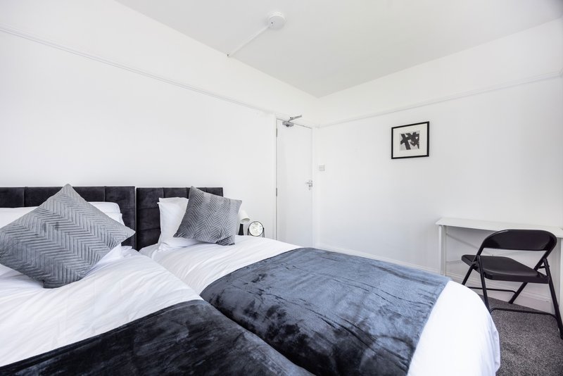 Modern bedroom with double bed, grey headboard, white bedding and folding chair