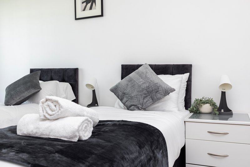 Modern bedroom with black bed frame, white and gray bedding, rolled towels and decorative pillows