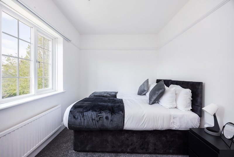 Bright bedroom with double bed, black headboard, white bedding and dark throw blanket